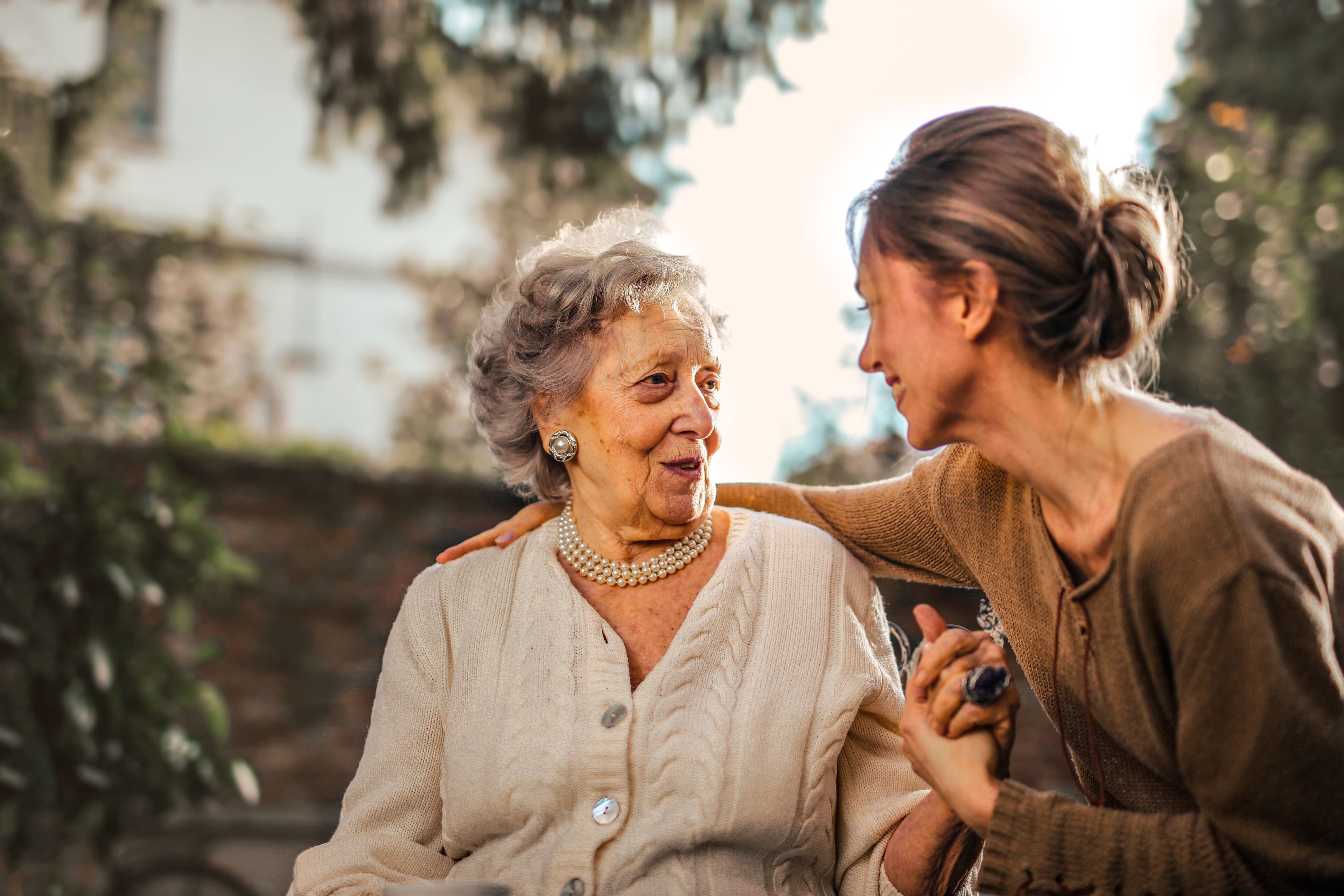 An older woman and a younger caregiver sharing a warm moment outdoors